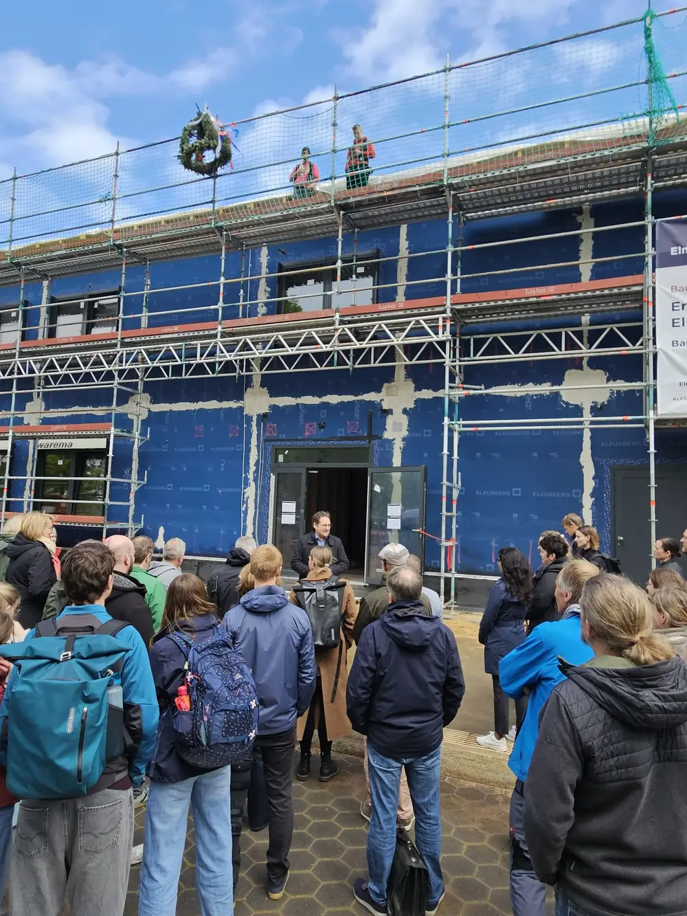 Die Schulleitung stellt den Neubau vor. Am oberen Ende des Gerüsts ist die Richtkrone befestigt.